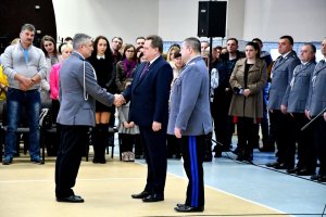 Wiceminister Spraw Wewnętrznych i Administracji gratuluje nowemu komendantowi w Sokółce. W tle kadra kierownicza policji i bliscy oraz rodziny nowoprzyjetych policjantów.