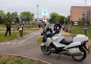na pierwszym planie policyjny motocykl, w tle dziewczynka jadąca po torze dla rowerów.  po bokach dwóch policjantów