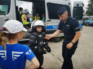 umundurowany policjant oraz dziecko ubrane w kamizelkę szturmową oraz ochraniacze, kask