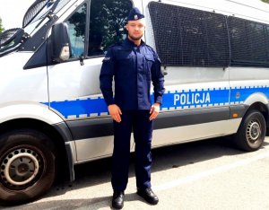Policjant z Oddziału Prewencji Policji w Białymstoku stoi na tle radiowozu mercedes sprinter.