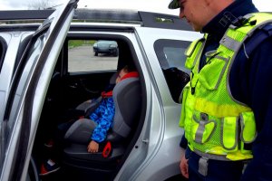 umundurowany policjant obok pojazdu. w pojezdzie dziecko siedzące w foteliku