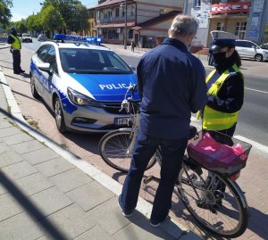 Policjanci kontrolują rowerzystę. W tle policyjny radiowóz.