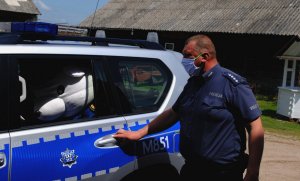 Policjant otwiera drzwi radiowozu dla policyjnej maskotki.