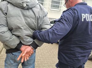 policjant prowadzi osobę zatrzymaną, która ma kajdanki na rękach trzymanych z tyłu