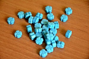 niebieskie tabletki ecstazy w kształcie czterolistnej koniczyny, rozsypane na brązowym blacie