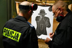 dwóch policjantów, którzy stoją przy tarczy strzeleckiej, po wykonanym strzelaniu