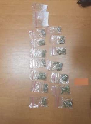 Zdjęcie w kolorze. Na pierwszym planie -  ujawnione przez policjantów środki odurzające podczas interwencji, mianowicie:  14 torebek strunowych z zawartością suszu roślinnego - marihuany i 3 torebki strunowe z białym proszkiem - amfetamina.