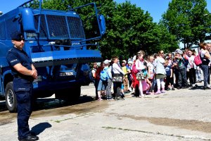 Dzieci zwiedzają policyjna armatkę wodną, przy której stoi policjant.