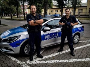dwóch umundurowanych policjantów, którzy stoją przy radiowozie