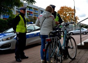 Dwóch umundurowanych policjantów i obok kobieta z miętowym rowerem
