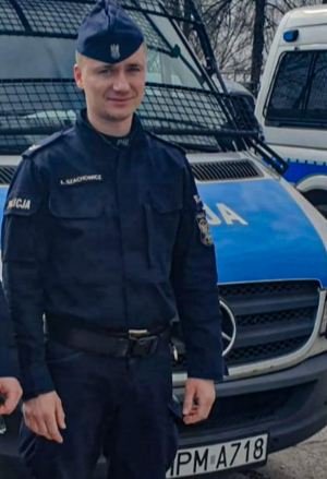 Policjant z OPP w Białymstoku na tle radiowozu.