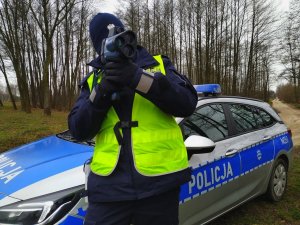 umundurowany policjant z wideorejestratorem w rękach, stojący przy radiowozie