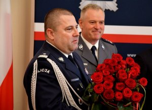 Komendant Wojewódzki Policji z bukietem róż. W tle zastępca komendanta.