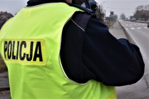 mężczyzna w granatowym mundurze i żółtej kamizelce z napisem policja