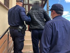 policjanci w mundurach prowadzą po schodach mężczyznę w czarnej kurtce