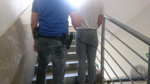 Nieumundurowany policjant prowadzi po schodach zatrzymanego mężczyznę.