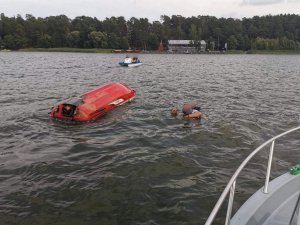 Skuter wywrócony na jeziorze, a w wodzie dwóch mężczyzn.