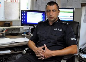 Policjant siedzi na krześle przed monitorem komputera.