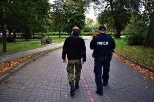 Policjant z żołnierzem idą alejką w parku