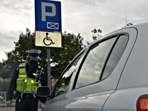 Policjant kontroluje pojazd zaparkowany na miejscu parkingowym dla niepełnosprawnych