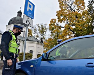 Policjant kontroluje pojazd zaparkowany na miejscu parkingowym dla niepełnosprawnych