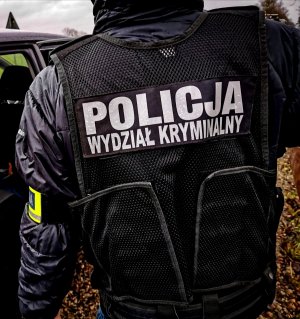 policjant na zewnątrz w kamizelce taktycznej z napisem POLICJA WYDZIAŁ KRYMINALNY