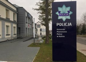 Tablica informacyjna z napisem Policja Komenda Powiatowa Policji w Kolnie a w tle budynek jednostki.