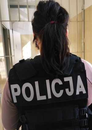 Kobieta w kamizelce z napisem Policja stoi tyłem