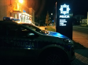 radiowóz na zewnatrz; pora wieczorowa; w tle budynek i ulica