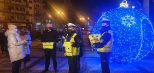 Policjantki stoją wraz z innymi osobami obok świecących na niebiesko obiektach.