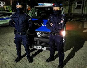 Dwóch policjantów stoi przed radiowozem po zmierzchu.