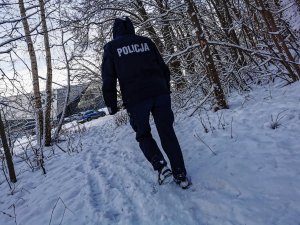 osoba w mundurze z napisem policja na plecach obok drzewa na ziemi śnieg