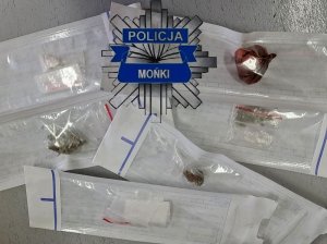 Gwiazda policyjna z napisem Policja a poniżej Mońki. Poniżej papierowe woreczki z narkotykami.