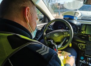 Policjant siedzi za kierownicą radiowozu i pisze.
