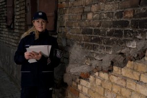 Policjantka trzyma dokumenty. Za nią stare budynki.