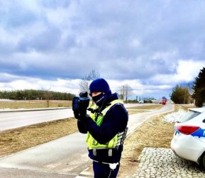 policjant dokonuje pomiary prędkości; w tle droga, niebo