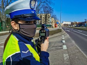 policjantka ruchu drogowego przed pomiarem prędkości; w tle ulica, budynki oraz niebo