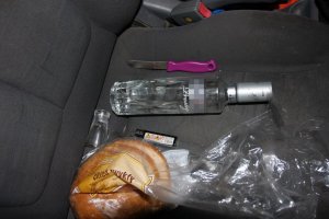 Butelka po alkoholu na siedzeniu w aucie, chleb i zapalniczka.