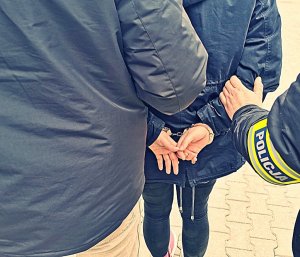 dwóch policjantów po cywilnemu prowadzi zatrzymaną; zbliżenie na ręce kobiety w kajdankach