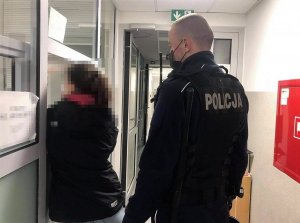 Kobieta stoi przy drzwiach a obok policjant.
