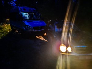 Pojazd typu bus z napisem policja a przed nim stoi pojazd osobowy z włączonymi światłami w porze nocnej.