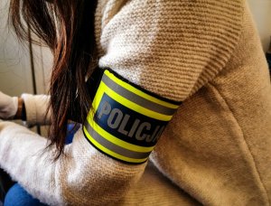 ramię kobiety na ramieniu opaska z napisem policja na ramię opadają ciemne włosy