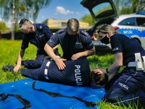 Policjanci, którzy udzielają pomocy leżącej osobie w ramach szkolenia z zakresu udzielania pierwszej pomocy.