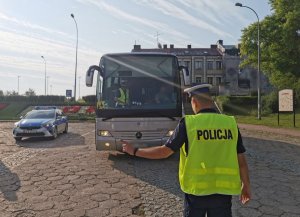przed autobusem mężczyzna w kamizelce odblaskowej z napisem policja