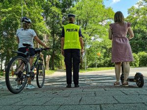 Policjantka a bok niej rowerzysta i dziewczynka na hulajnodze