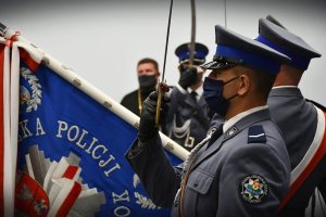 Policjanci trzymają uniesione szable i sztandar.
