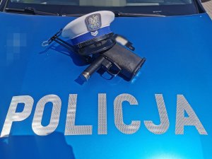 granatowa maska samochodu napis policja powyżej czapka z białym pokrowcem i miernik prędkości