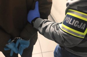 widok na ramię na ramieniu opaska z napisem policja obok osoba trzymająca ręce za plecami na nadgarstkach kajdanki