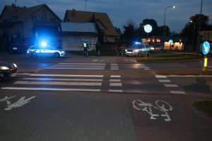 ulica w mieście wieczorem widok na przejście dla pieszych i przejazd dla rowerów na jezdni stojące samochody policji