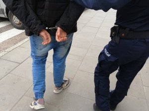 widok na mężczyzn 1 w kajdankach obok drugi w spodniach z napisem policja